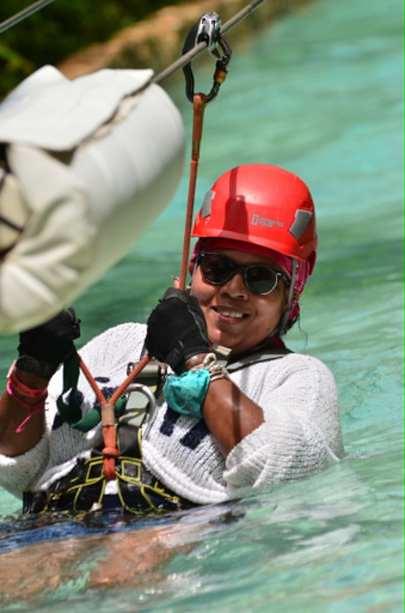 Woman ziplining over turquoise water wearing red helmet